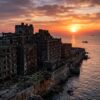 Abandoned concrete buildings on island coastline at sunset with boats on ocean
